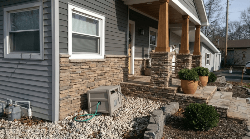 Stone siding around a front porch with stacked stone columns and gray house exterior